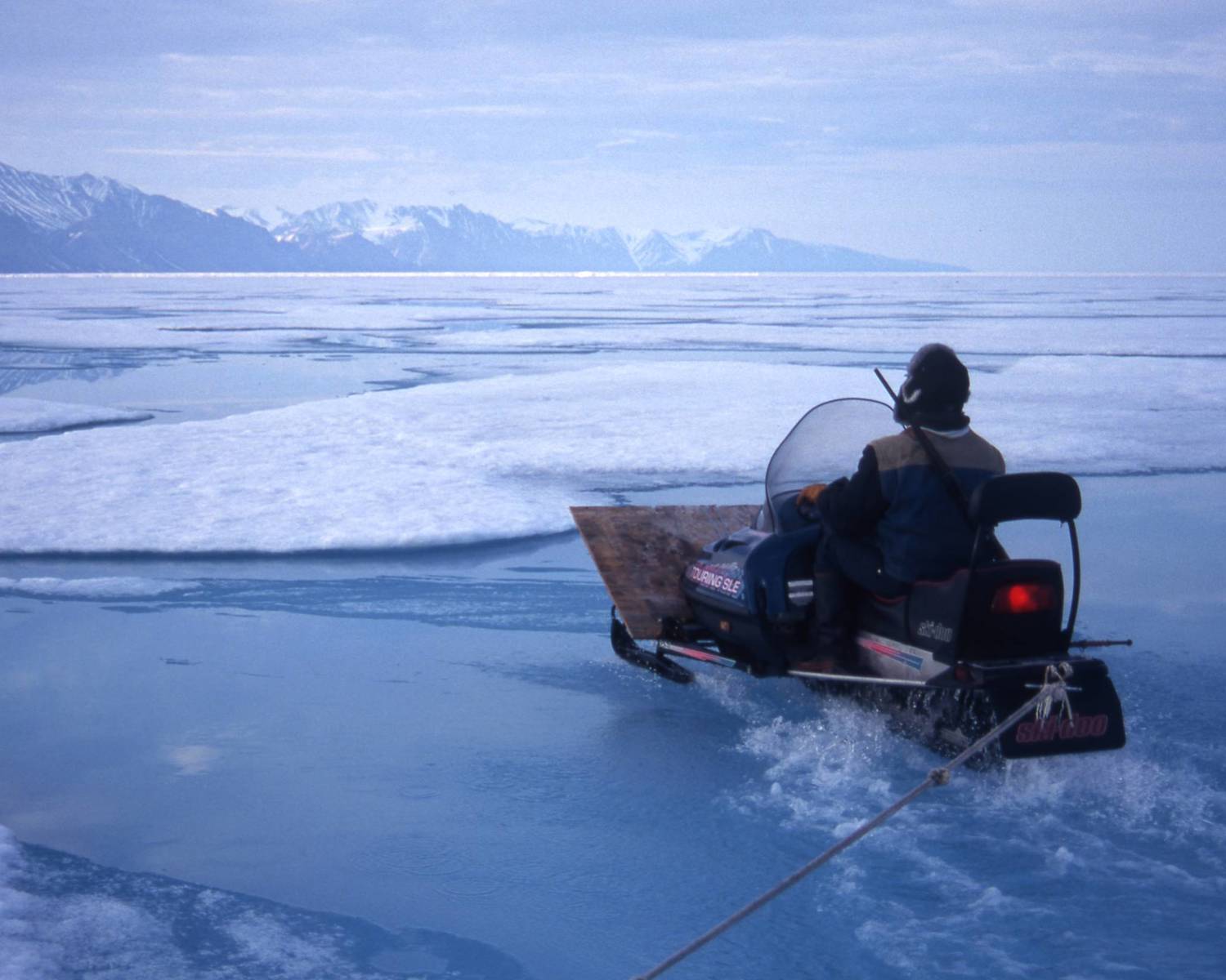 Inuit hunter traveling by snow scooter on melting sea ice, Pond Inlet, Canada